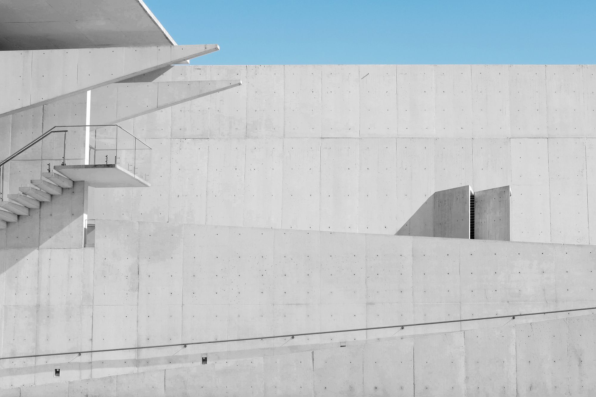 Pale board-marked concrete walls and a cantilevered stair against a blue sky