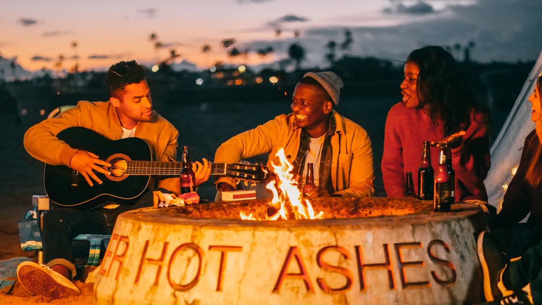 Friends around a campfire with a guitar at dusk